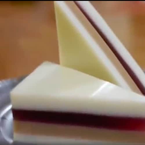 Smooth, glassy peanut butter and jelly sandwich cut on the diagonal. One half of sandwich lays flat on gray plate, the othe half is standing up next to it.