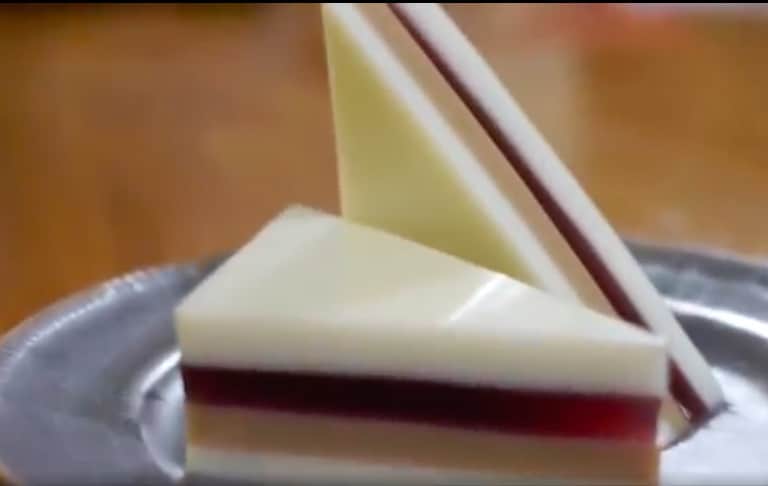 Smooth, glassy peanut butter and jelly sandwich cut on the diagonal. One half of sandwich lays flat on gray plate, the othe half is standing up next to it.