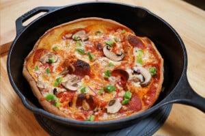 A pizza topped with mushrooms, pepperoni, bell peppers, and cheese in a cast iron pan.