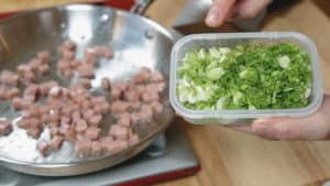 Chopped green onion and spam in a skillet.