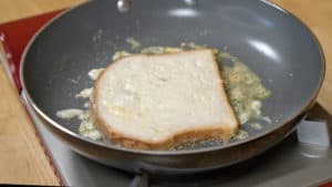 A slice of cream soaked bread frying in butter in a non-stick skillet.