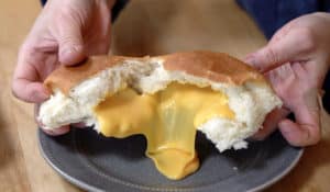 Hands splitting apart white bun with orange American cheese oozing out.