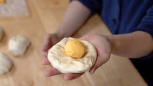 Open hand holding a round flat of dough with an orange ball of Velveeta cheese on top.