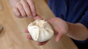 Open palm holding a packet of dough with the edges gathered up and pushed together.
