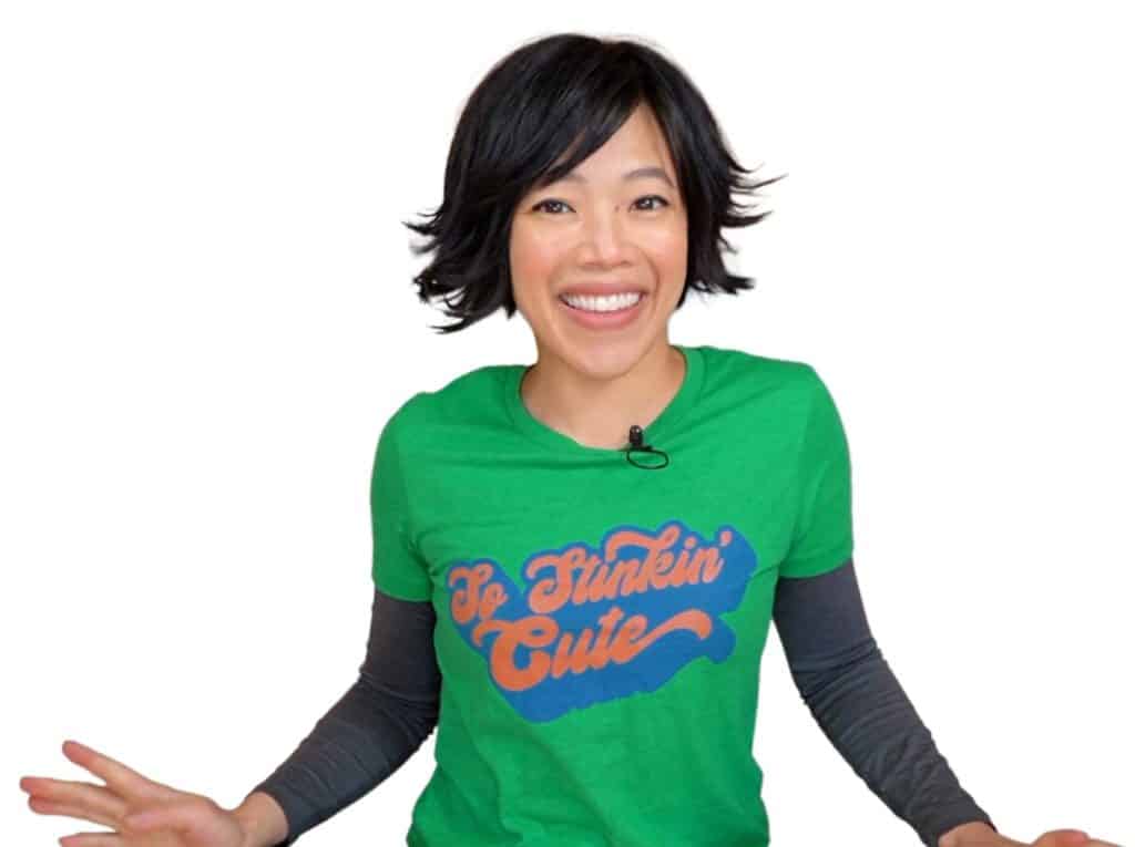 A woman with short black hair wearing a green tee shirt that says 'so stinkin' cute'.