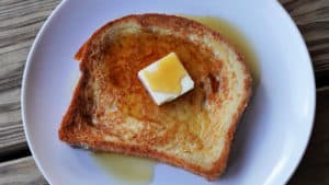 A slice of french toast topped with a pat of butter and maple syrup.