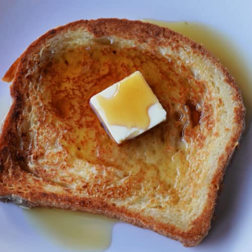 A slice of french toast topped with a pat of butter and maple syrup.