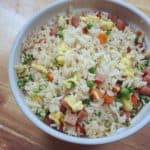 A bowl of rice rice contain peas, carrots and spam.