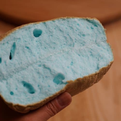 A hand holding a blue cloud bread torn in half.