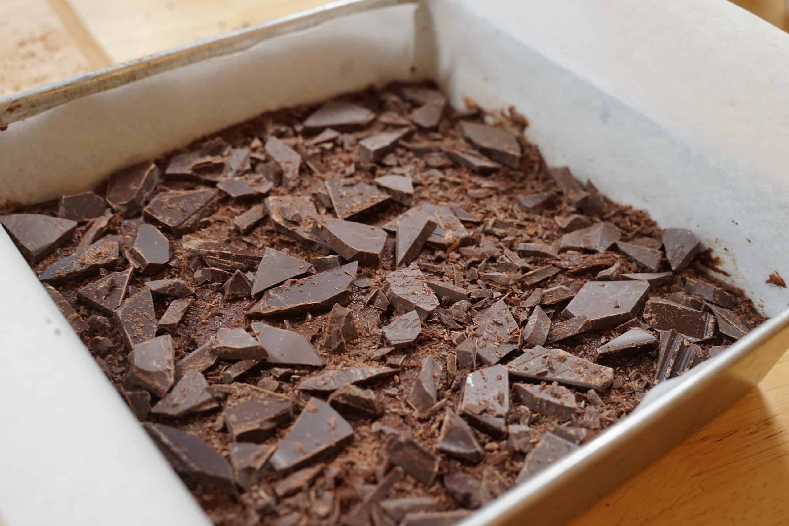 An unbaked batch of brownies topped with shards of dark chocolate. 