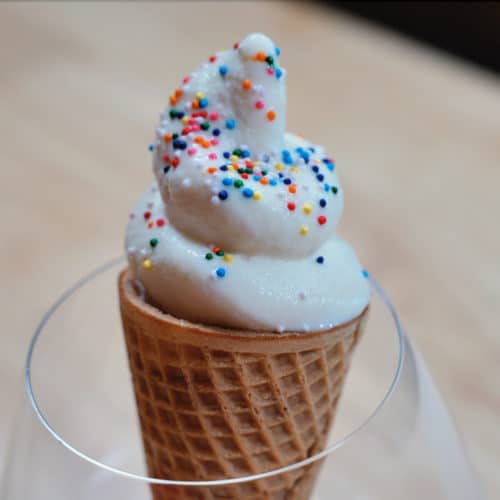 A swirl of soft serve ice cream topped with rainbow sprinkles.