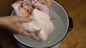 Placing a raw chicken into a pot of water.