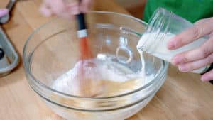 Pouring milking into a bowl while whisking.