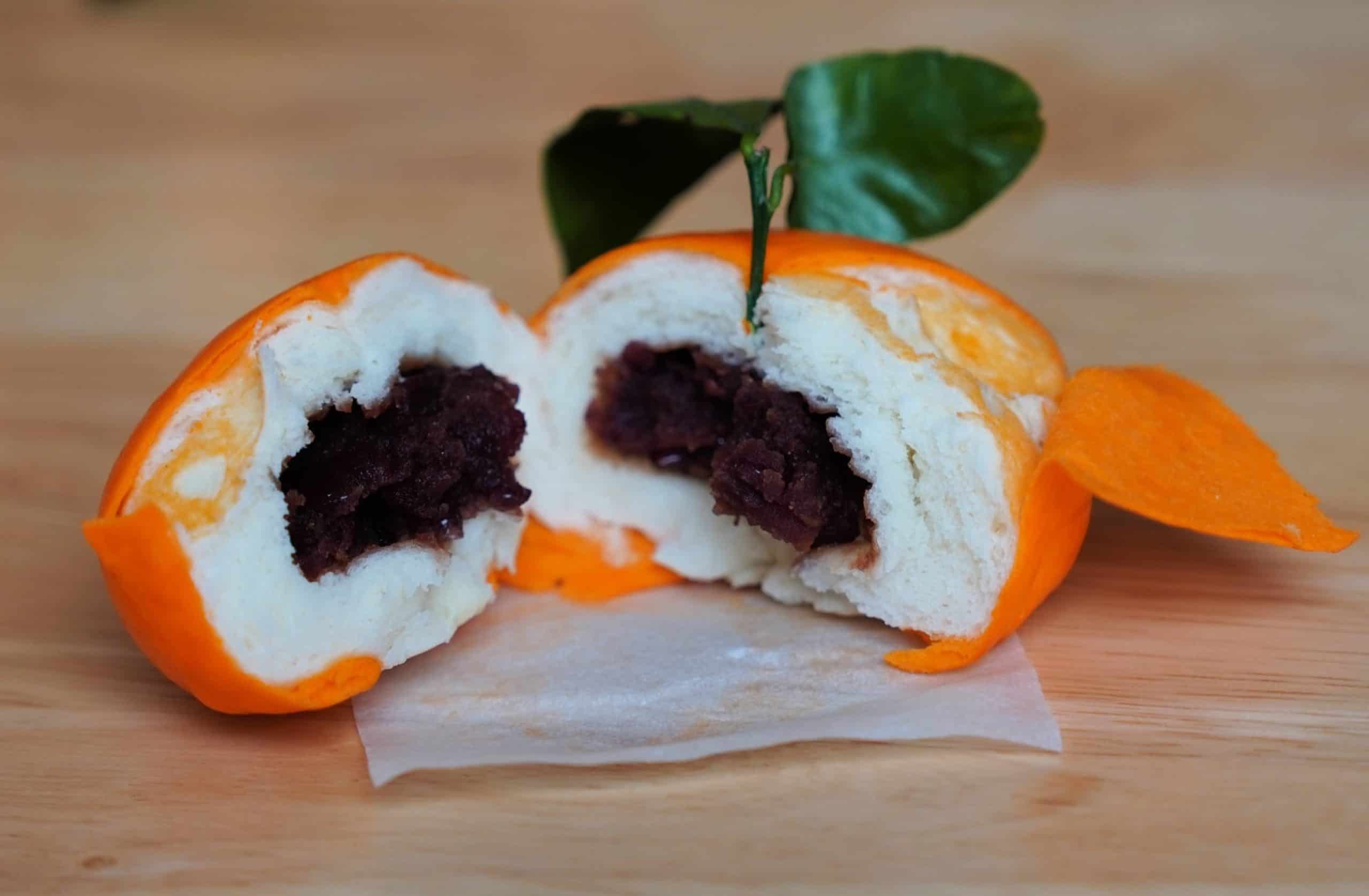 A tangerine bao torn open displaying the red bean paste inside. 