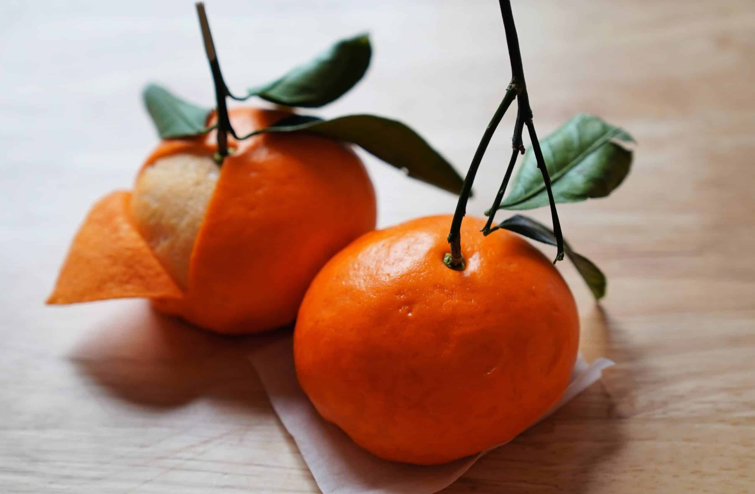 Two steamed buns that look like tangerine, one is peeled revealing the interior. 