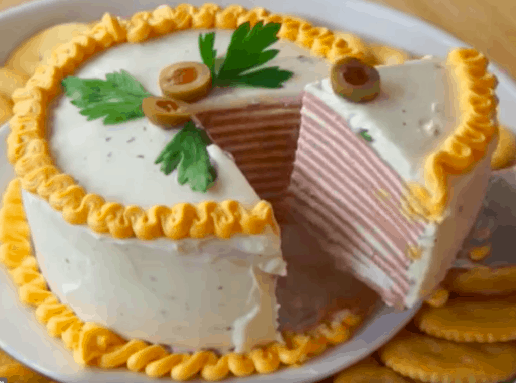 There is a "cake" sliced with one piece on a serving utensil. The cake consists of layers of bologna and frosting.