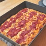 A rectangular pan of Detroit pizza topped with red sauce and cheese.