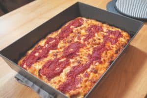 A rectangular pan of Detroit pizza topped with red sauce and cheese.