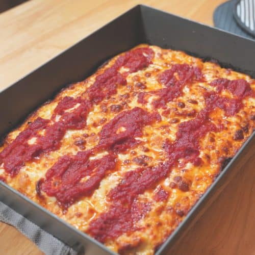 A rectangular pan of Detroit pizza topped with red sauce and cheese.