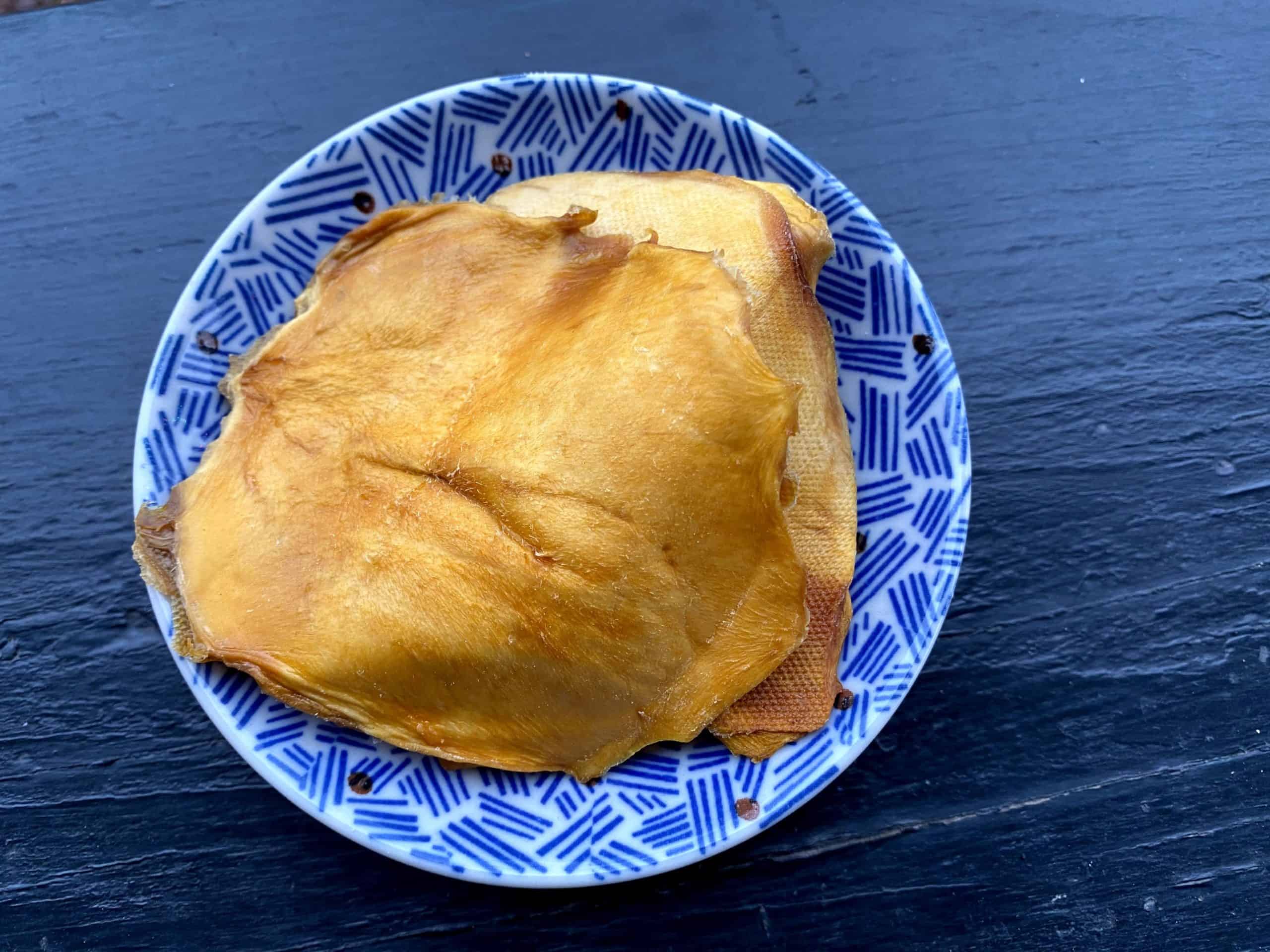 Orange unsweetened dried mango slices on a blue and white saucer on a black background.