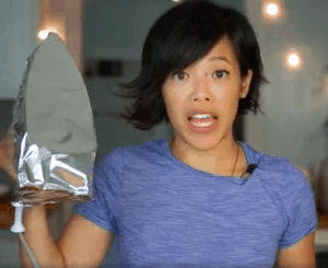 Woman in blue t-shirt holding up an iron wrapped in aluminum foil.