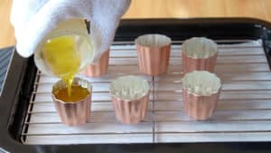 Pouring melted beeswax into a canelé mold.