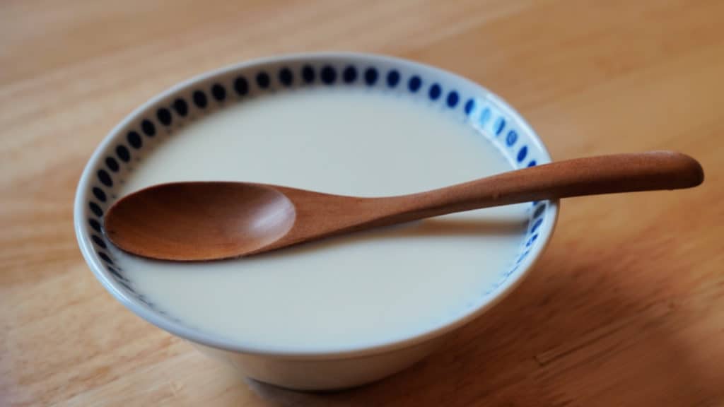 A bowl of ginger milk curd with a wooden spoon.