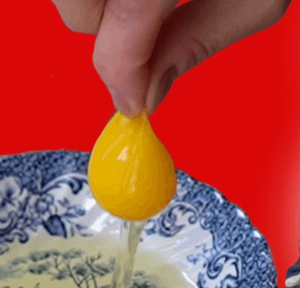 Thumb and forefinger pinching and holding up egg yolk with white dripping down into dish.