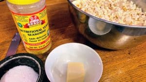 Small white bowl of butter; small black bowl of salt; jar of Bragg's nutritional yeast; bowl of popcorn.