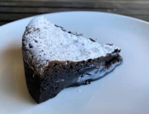 A slice of gooey chocolate cake covered with powdered sugar.