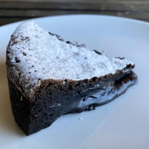 A slice of gooey chocolate cake covered with powdered sugar.