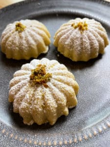 Three maamoul cookies dusted with powdered sugar and topped with chopped pistachios.