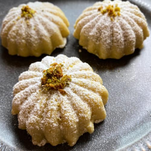 Three maamoul cookies dusted with powdered sugar and topped with chopped pistachios.