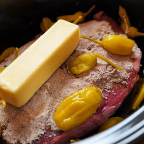A stick of butter and pepperoncini peppers on a chuck roast.