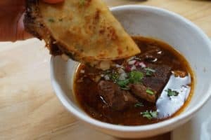 Taco being dipped into a bowl of dark stew.