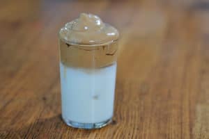 A glass of milk with Dalgona whipped topping on top third.
