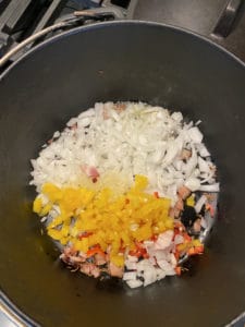 White onion, yellow bell pepper, and red chili pepper sautéing in cast iron pot.