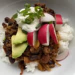 Bison bean chili over a bed of rice topped with radishes, avocado, sour cream, and green onions.