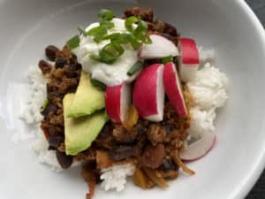 Bison bean chili over a bed of rice topped with radishes, avocado, sour cream, and green onions.