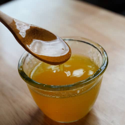 A wooden spoon scooping corn cob honey.y.