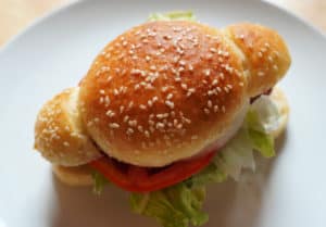 A hamdog topped with lettuce, tomato, and onion on a sesame seed bun.