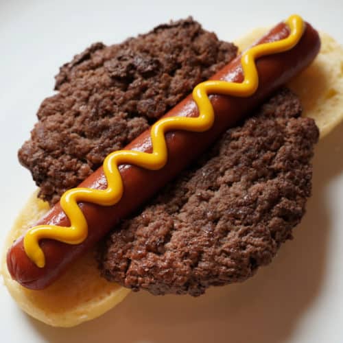A hamburger patty and a hot dog or hamdog on a bun with a squiggle of mustard.