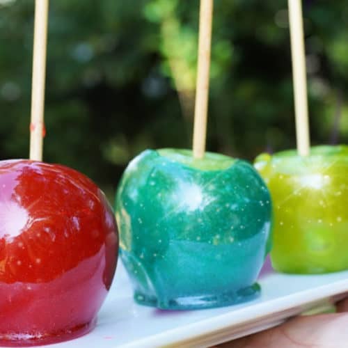 A red, a blue, and a green candy apple sitting on a white plate.