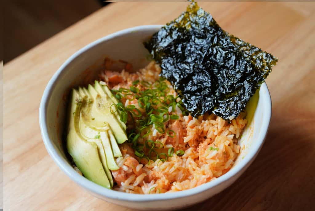 A salmon rice bowl topped with sliced avocado and nori seaweed.