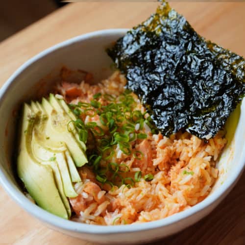 A salmon rice bowl topped with sliced avocado and nori seaweed.