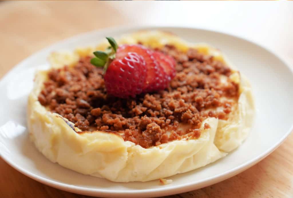 Cheesecake on a white plate topped with cookie crumbles and slice strawberries.