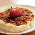 Cheesecake on a white plate topped with cookie crumbles and slice strawberries.