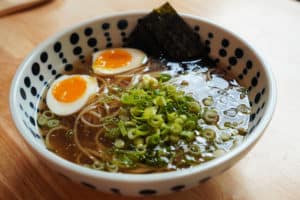 A large bowl of soy sauce ramen with green onions and soft-boiled eggs.