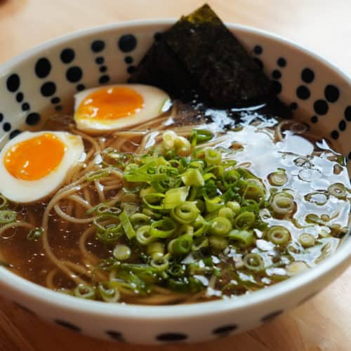 A large bowl of soy sauce ramen with green onions and soft-boiled eggs.