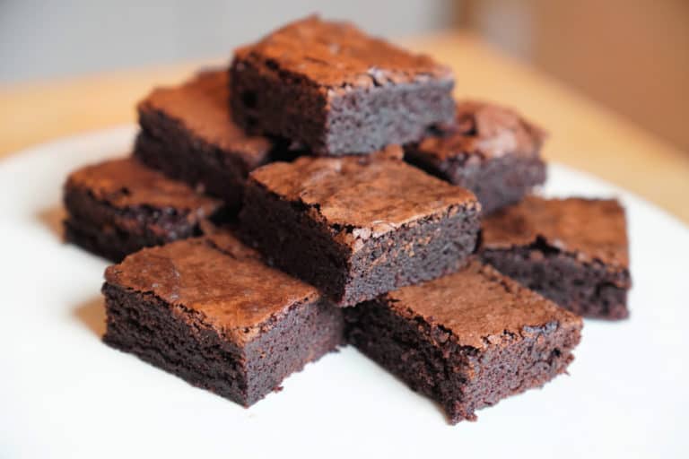Squares of brownies stacked on white plate.